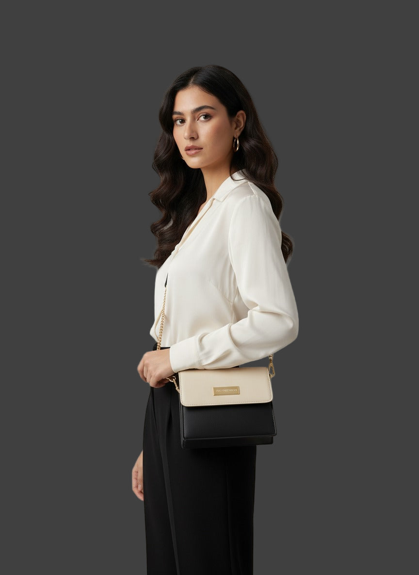 Woman holding a black handbag with a beige strap against a plain background