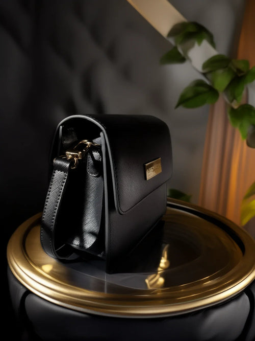 Black handbag with gold accents on a reflective surface
